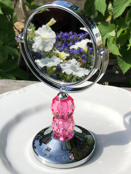 Compact mirror with pink handle reflecting flowers.