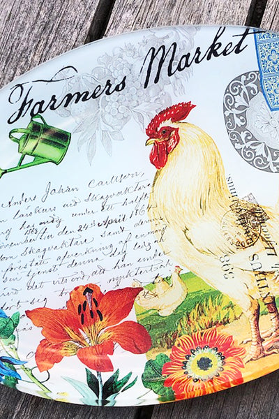 Decorative plate with a rooster, flowers, and 'Farmers Market' text on a wooden surface.