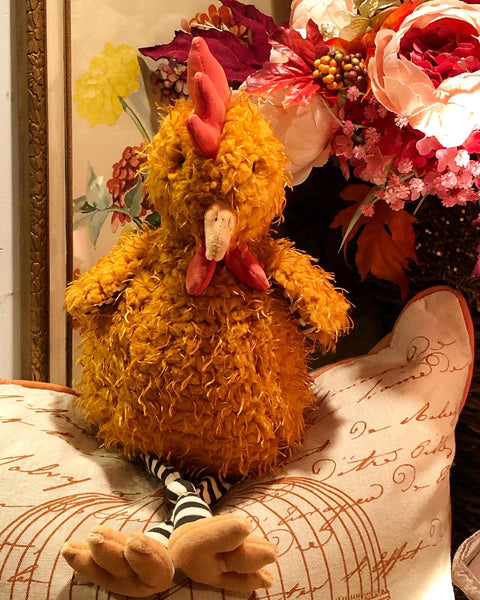 Plush rooster chicken stuffed animal on a decorative pillow with flowers in the background