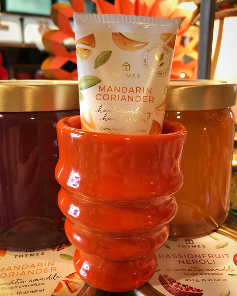 Hand cream with Mandarin Coriander scent in a vintage orange cup, surrounded by jars of candles.