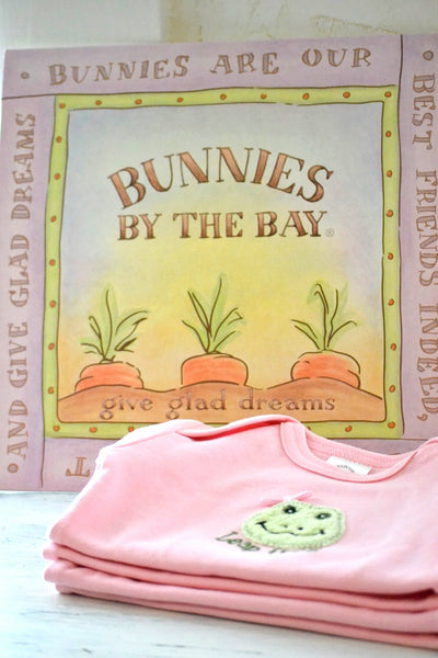 Pink baby onesie stack with a frog design in front of 'Bunnies by the Bay' sign
