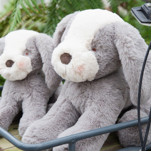Two gray stuffed dogs sitting in a basket with a green outdoor background