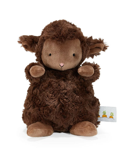 A plush sheep toy in dark brown with a lighter brown face, sitting against a solid white background. A small fabric tag with a carrot illustration is visible on the right side.