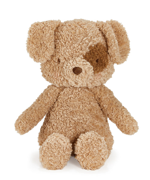 A plush teddy bear dog in a curly, bouclé-like fabric, featuring a light tan body with a darker brown patch over one eye and floppy ears, set against a plain white background.