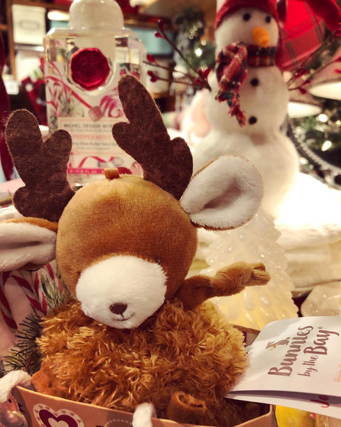 Plush reindeer toy with a snowman and product in the background