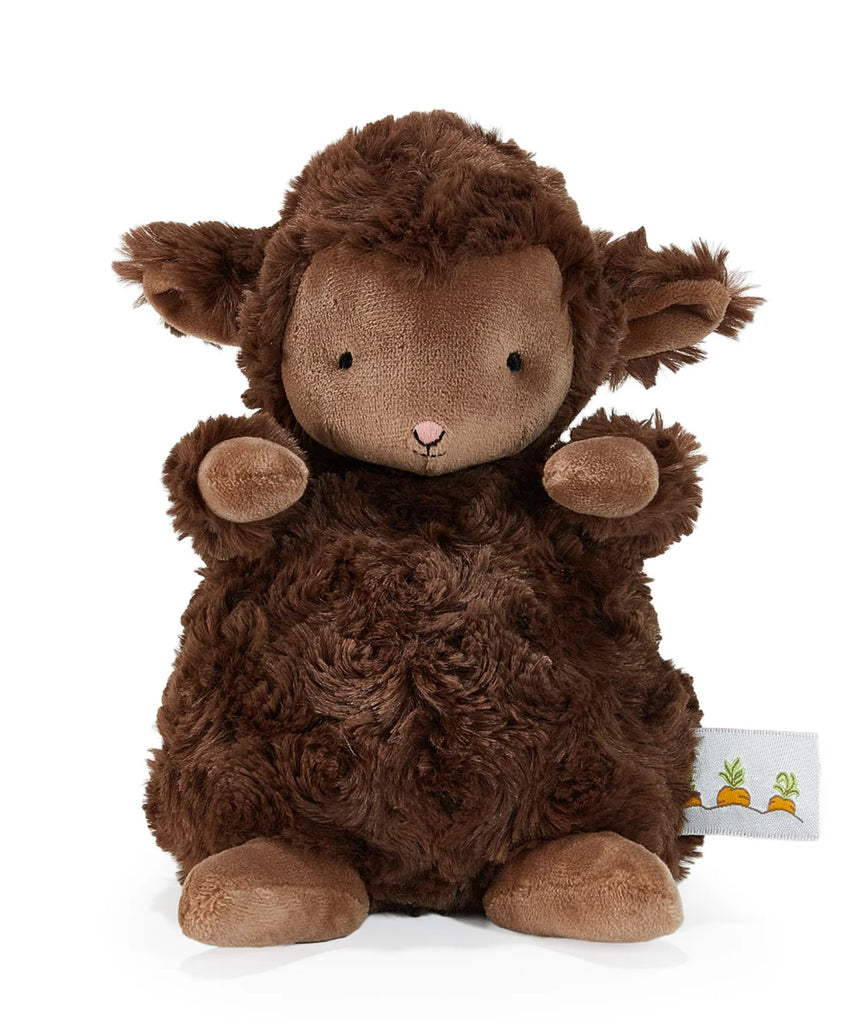 A plush brown sheep toy with curly textured fur, a light brown face, small black eyes, a pink stitched nose, and raised front paws, photographed on a clean white background. A small fabric tag with carrot illustrations is visible near the lower right.