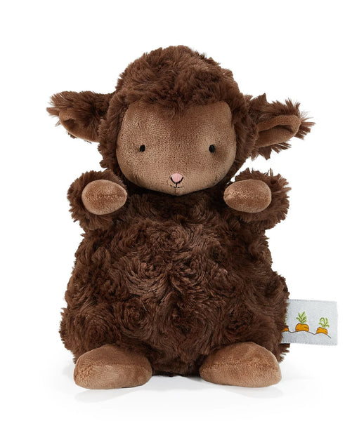 A plush brown sheep toy with curly textured fur, a light brown face, small black eyes, a pink stitched nose, and raised front paws, photographed on a clean white background. A small fabric tag with carrot illustrations is visible near the lower right.